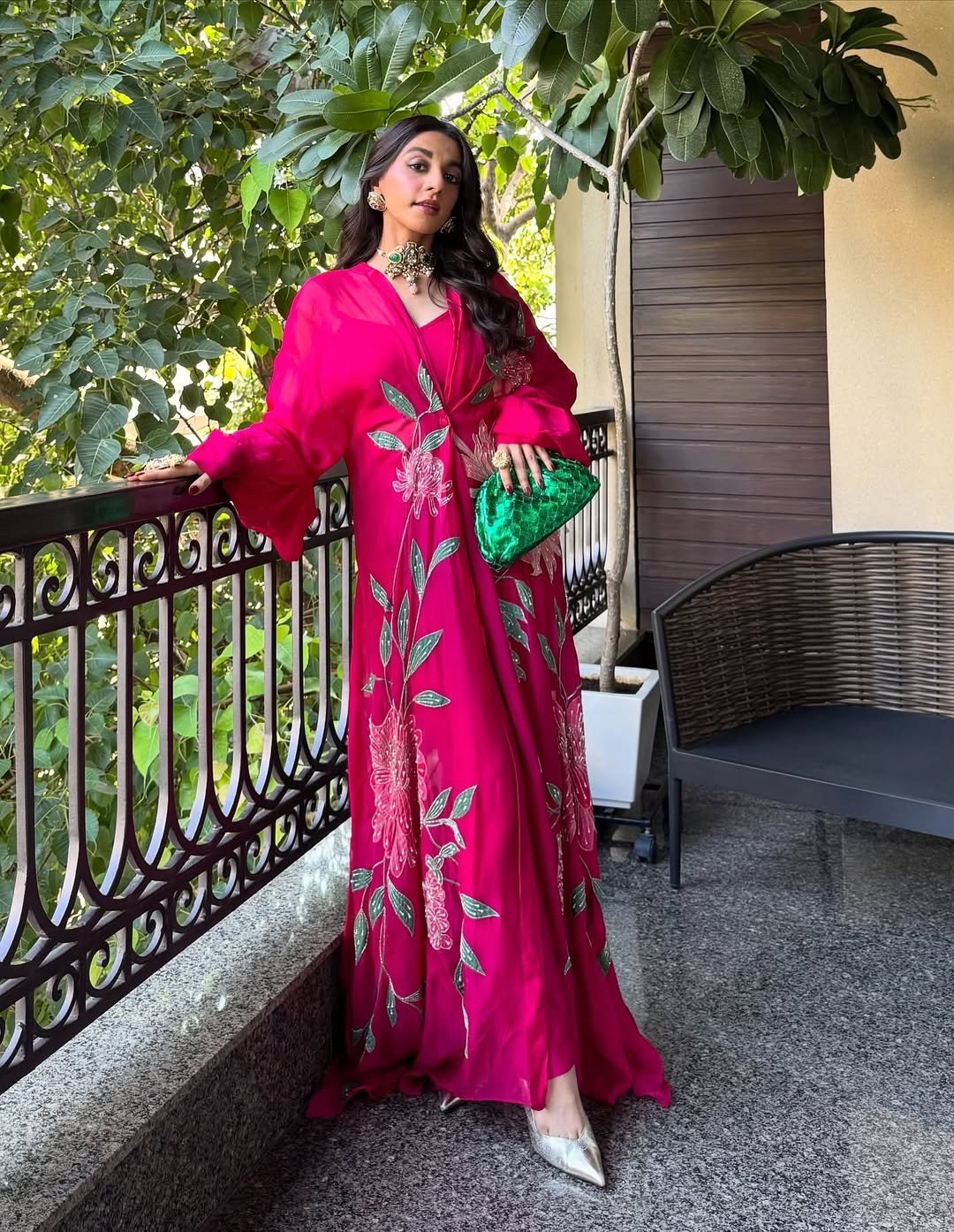 A hot pink long-sleeved dress with intricate floral embroidery and dramatic sleeves, paired with an emerald clutch.