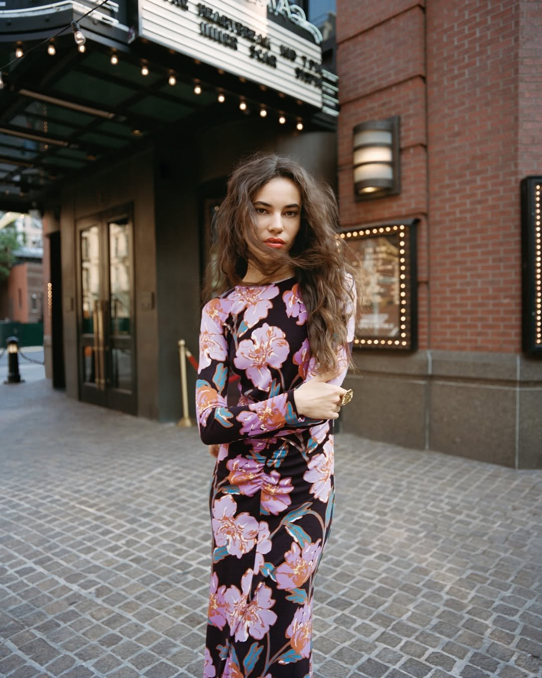 A body-skimming long-sleeve floral dress in bold pinks and purples against a city backdrop.