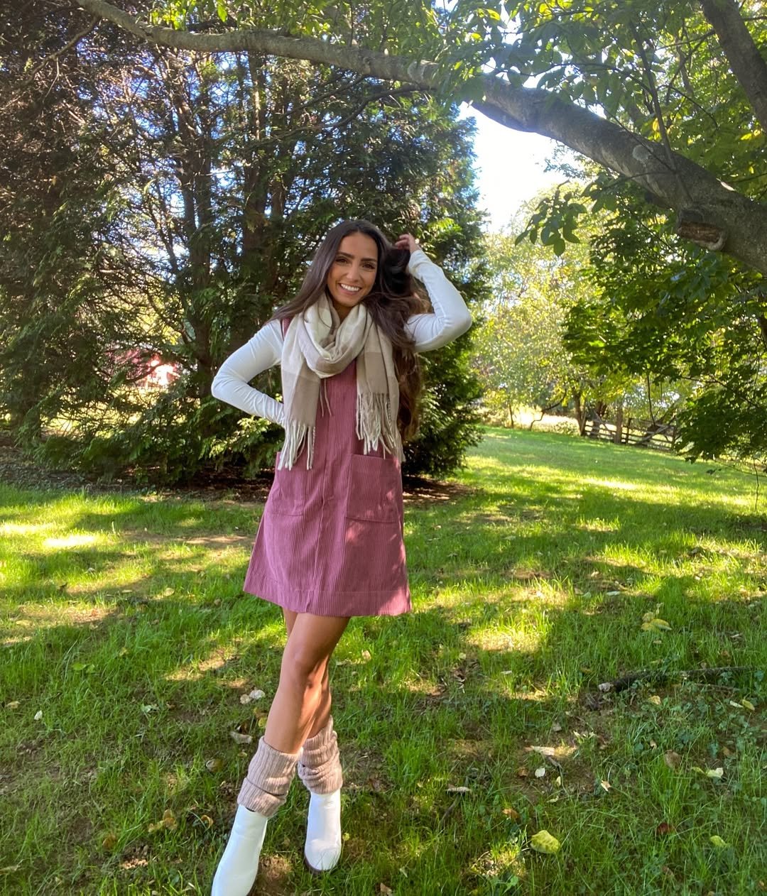 A corduroy pinafore layered over a fitted long-sleeve top, with a scarf, slouchy socks, and boots.