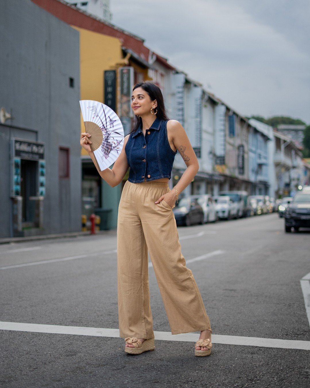 Woman wearing beige linen pants with a cropped denim vest and platform sandals.