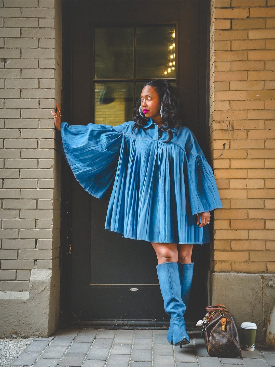 An oversized denim long-sleeved dress with exaggerated sleeves, paired with matching knee-high boots.