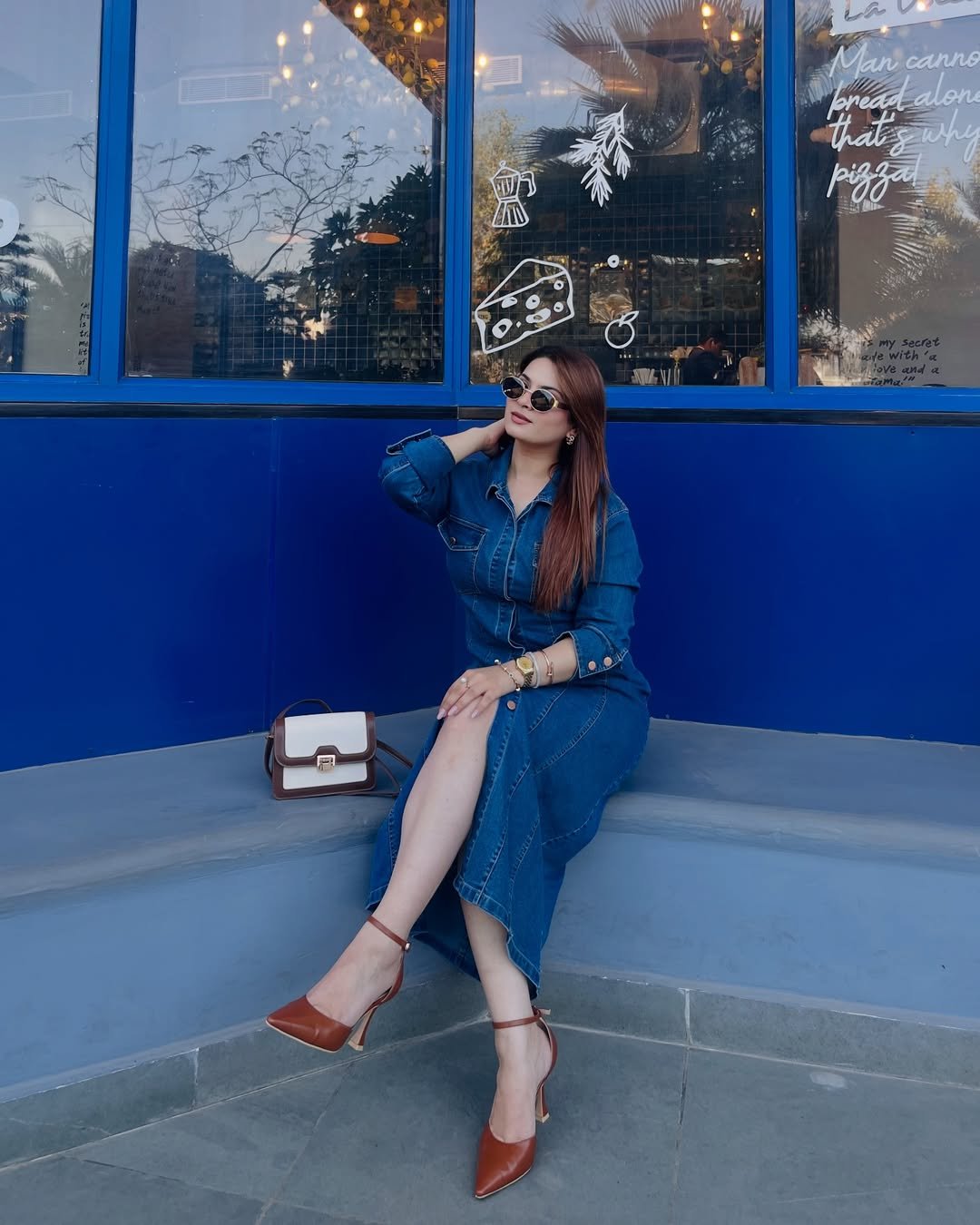 A denim midi dress with structured seams and a cinched waist, paired with pointed rust heels and sunglasses.