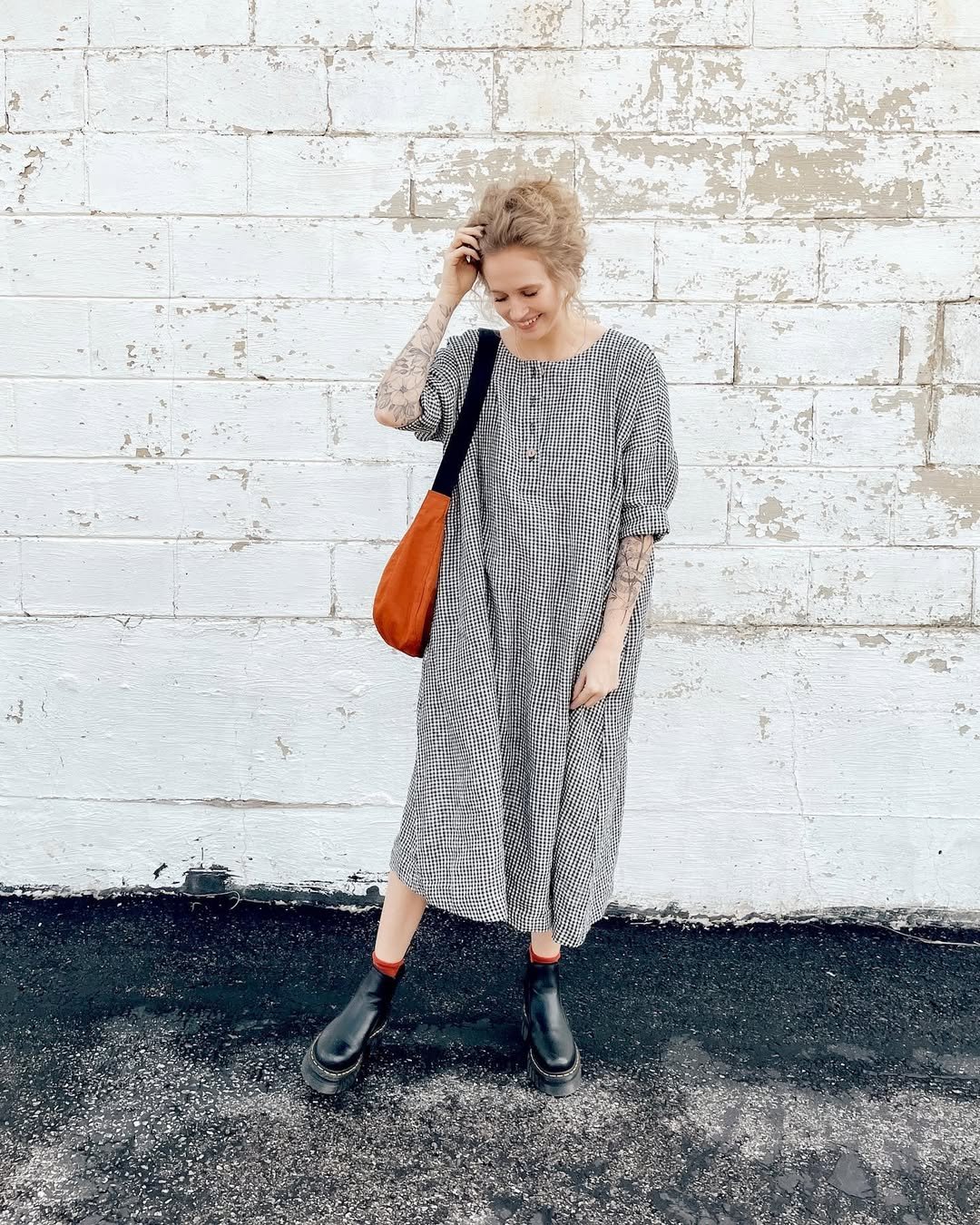 A woman wearing a loose-fitting, midi-length gingham dress with puff sleeves and chunky boots.