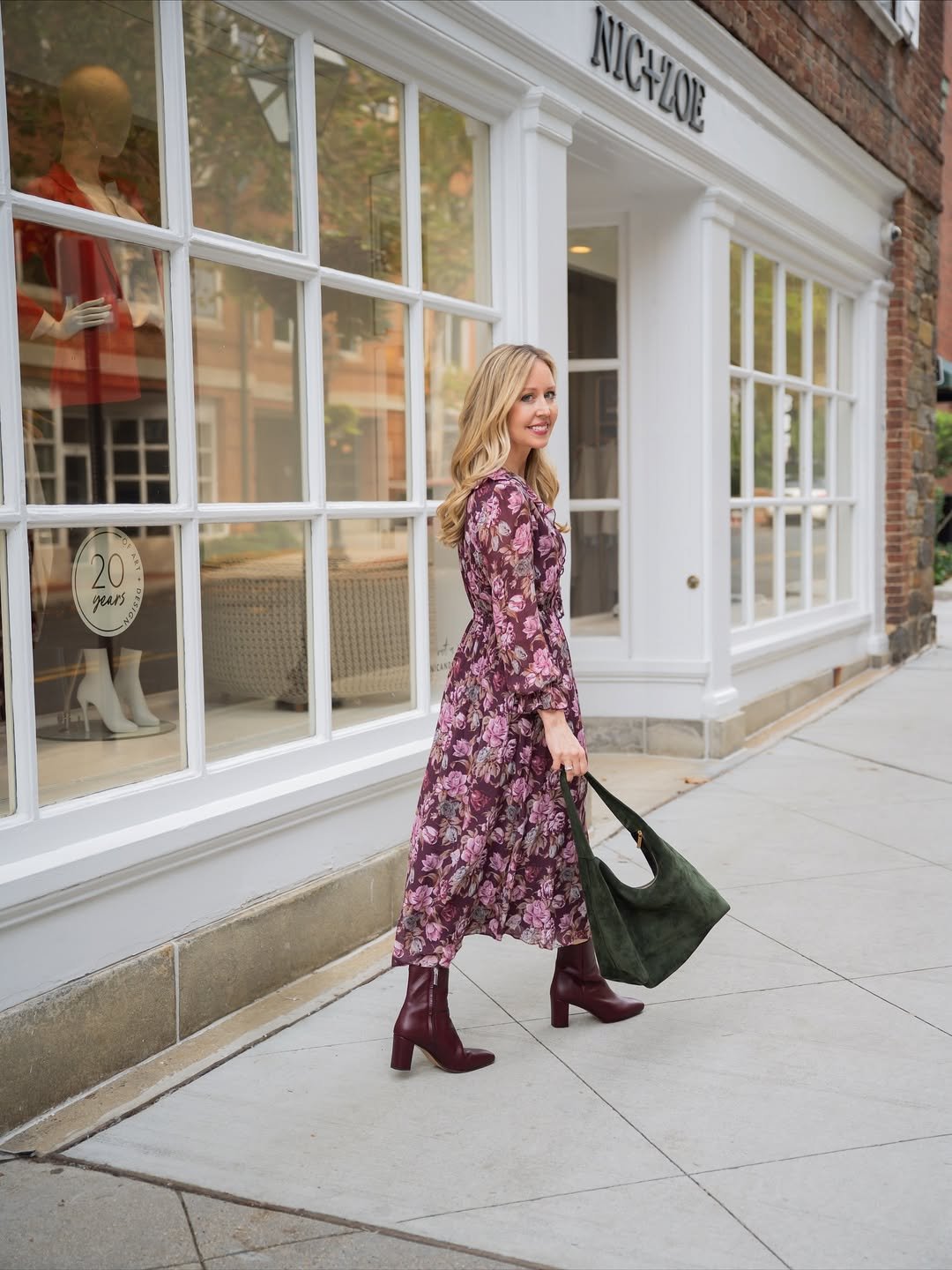 A long-sleeved floral midi dress in rich burgundy tones, cinched at the waist, with matching boots and a structured bag.