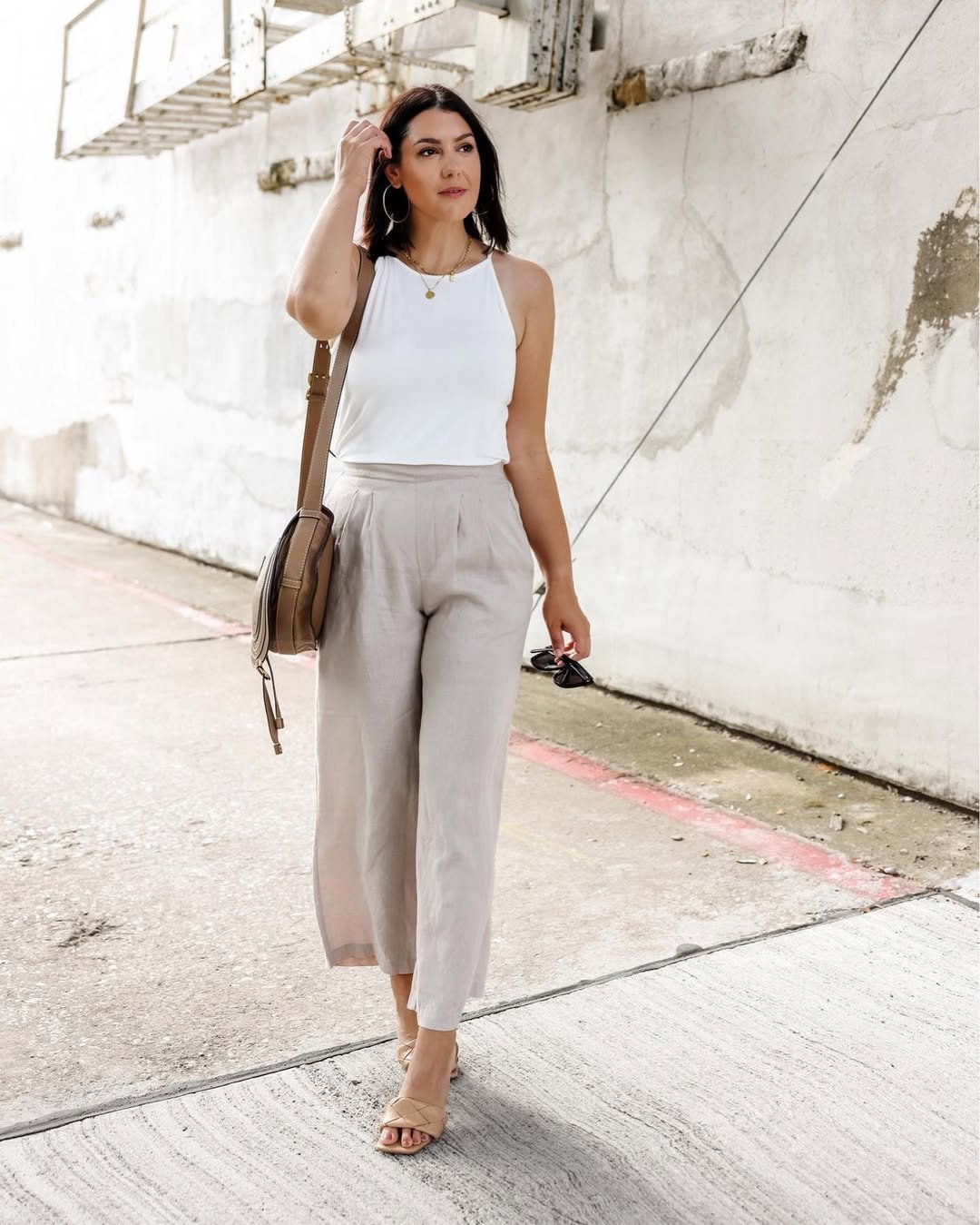 Woman wearing beige linen trousers with a white halter tank, tan slides, and a crossbody bag.