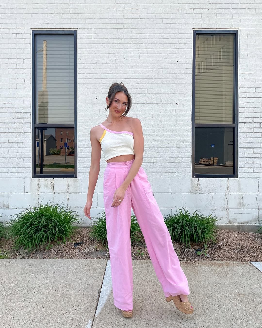 Woman wearing high-waisted pink linen pants with a one-shoulder pastel top.