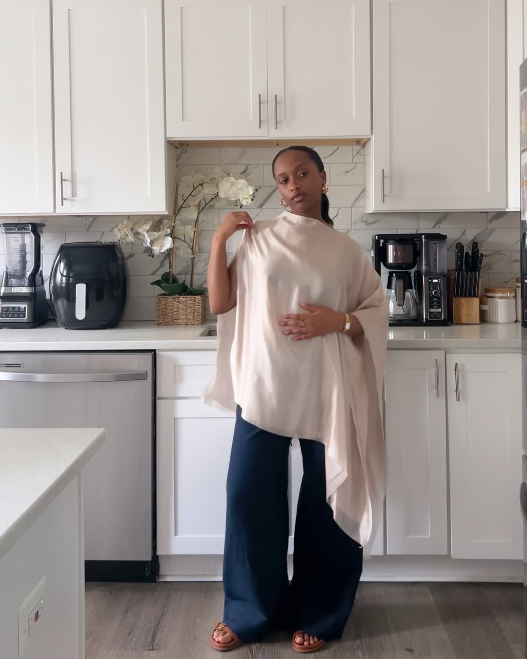 Woman wearing flowing navy linen pants with a draped beige asymmetrical top.