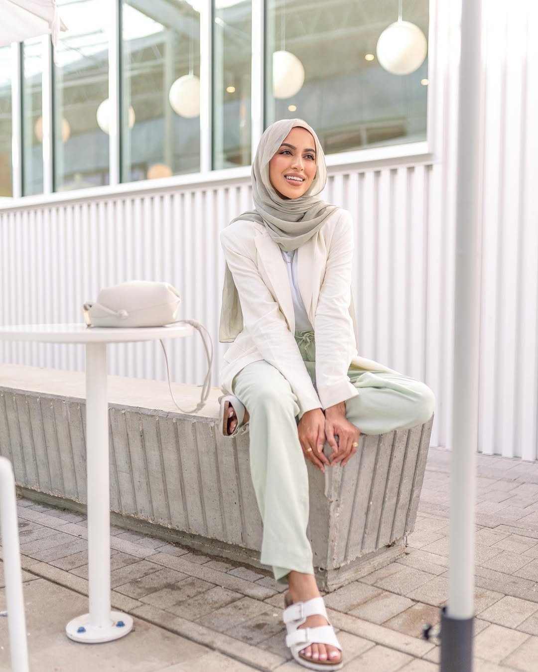 Woman wearing muted green linen pants with a cream blazer and white sandals.