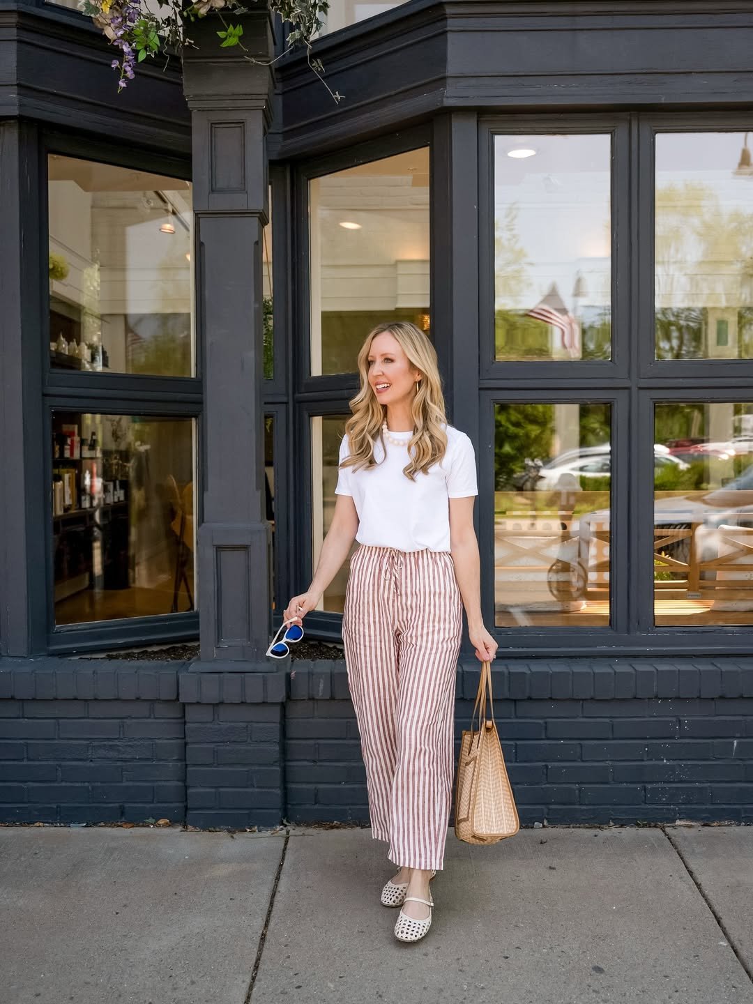 Woman wearing brown and cream striped linen pants with a white tee, woven tote, and Mary Jane flats.