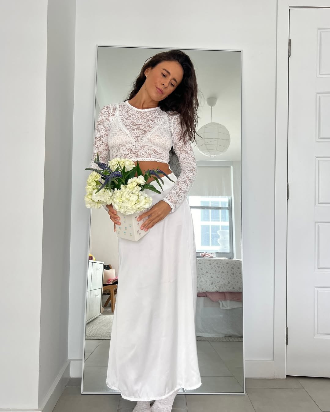 A delicate lace long-sleeved crop top layered over a silky white skirt, with loose hair.