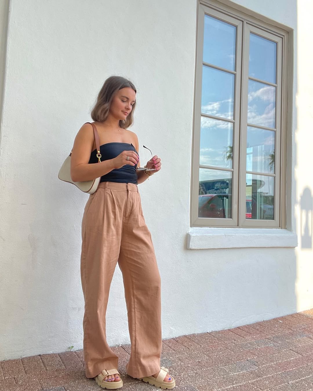Woman wearing camel linen pants with a black tube top and chunky sandals.