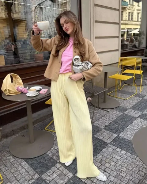 Woman in butter yellow trousers and pink tee at a Paris cafe