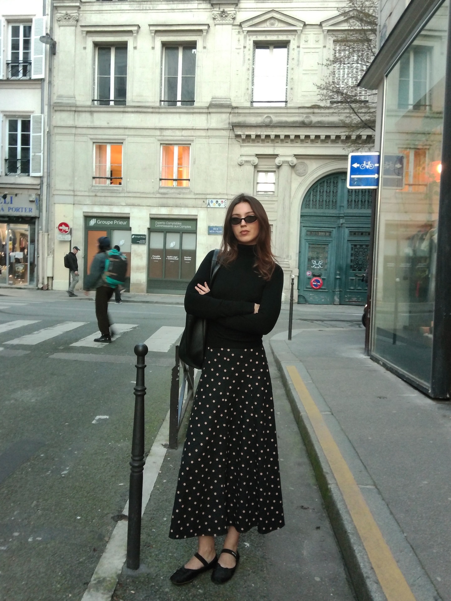 A woman wears a black turtleneck, a polka dot midi skirt, and Mary Jane flats.