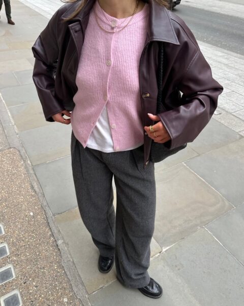 Plum leather jacket, pink cardigan, and pinstripe trousers.