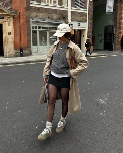 Tan overcoat, sweatshirt, micro-skirt, and trainers.