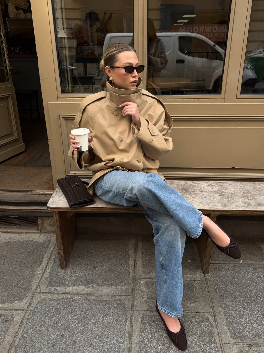 A woman wears a cropped high-neck trench coat with loose-fitting jeans and dark ballet flats.