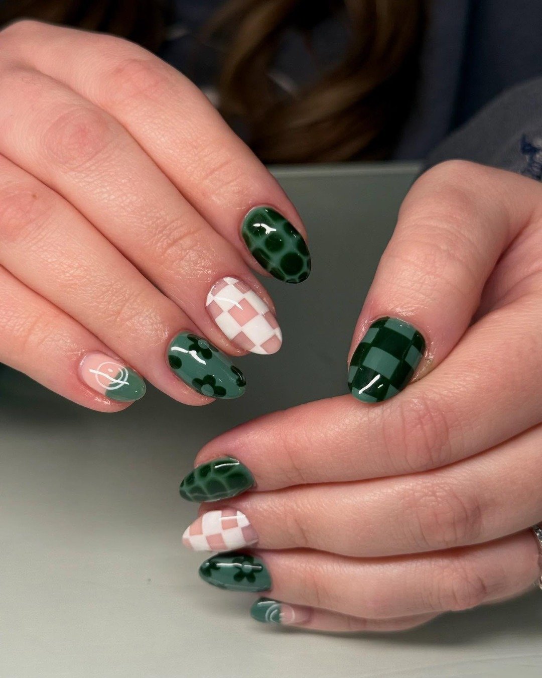 Nails with various patterns in deep green, including checkerboard and florals